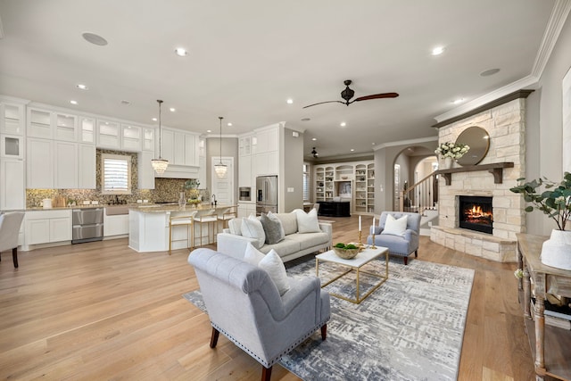 living room with crown molding, a fireplace, light hardwood / wood-style floors, and ceiling fan