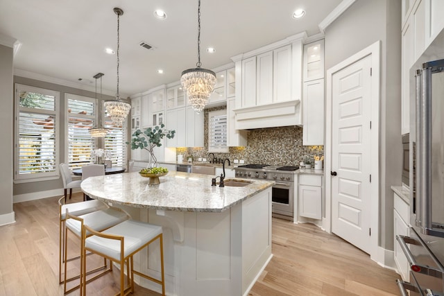 kitchen with stainless steel stove, white cabinetry, light stone counters, a center island with sink, and light wood-type flooring