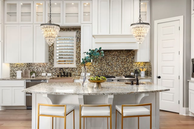 kitchen featuring pendant lighting, a kitchen island with sink, white cabinetry, light stone counters, and stainless steel dishwasher