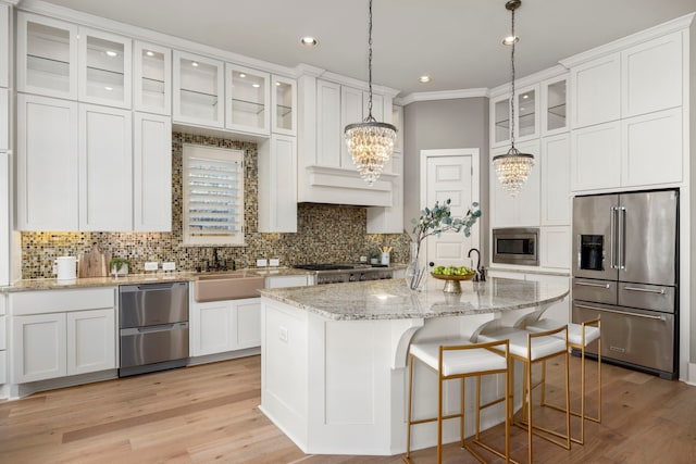 kitchen with white cabinetry, an island with sink, hanging light fixtures, stainless steel appliances, and light wood-type flooring