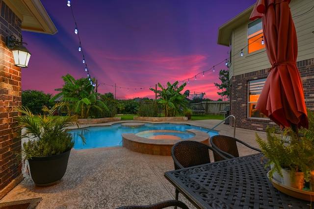 pool at dusk featuring a patio and an in ground hot tub