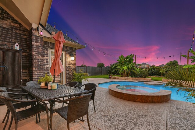 pool at dusk featuring an in ground hot tub and a patio