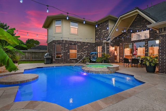 pool at dusk with a patio and an in ground hot tub