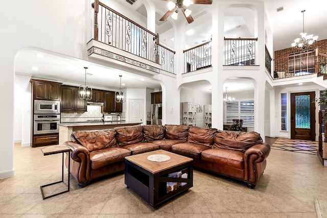 living room featuring ceiling fan with notable chandelier, a towering ceiling, and light tile patterned floors