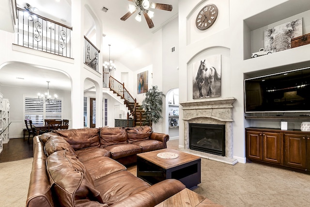 living room with a high end fireplace, crown molding, ceiling fan with notable chandelier, and a towering ceiling