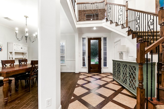 foyer entrance featuring wood-type flooring, a notable chandelier, crown molding, and a towering ceiling