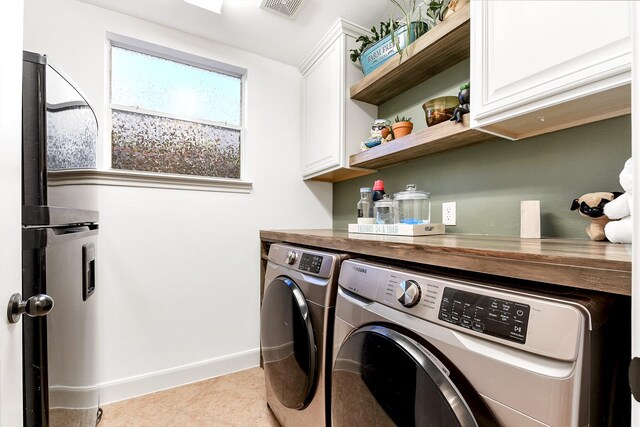 clothes washing area featuring washing machine and dryer, cabinets, and light tile patterned floors