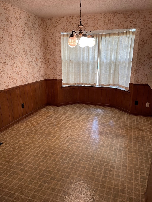 unfurnished room featuring wooden walls, a textured ceiling, and plenty of natural light