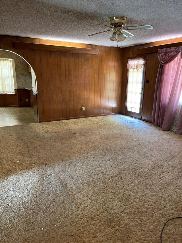 spare room featuring wood walls, a textured ceiling, carpet flooring, and ceiling fan