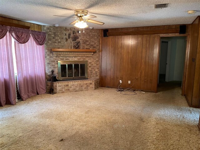 unfurnished living room featuring a fireplace, ceiling fan, carpet flooring, and wood walls