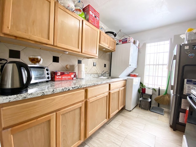 kitchen with tasteful backsplash, stainless steel fridge, sink, light stone counters, and stacked washer / drying machine