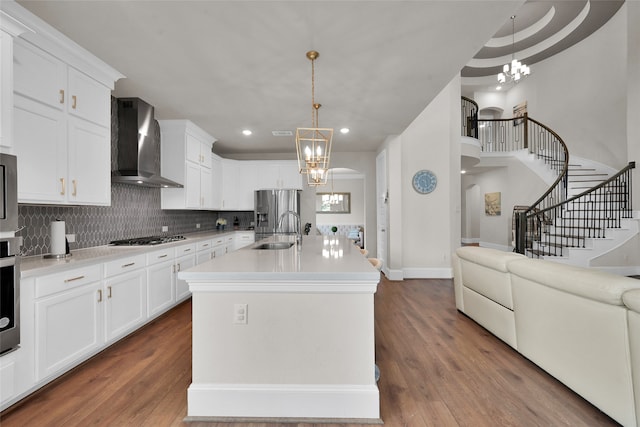 kitchen featuring hardwood / wood-style floors, wall chimney exhaust hood, sink, an inviting chandelier, and a kitchen island with sink