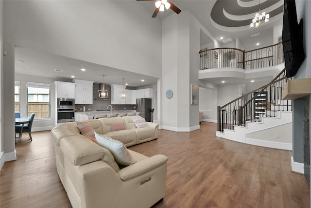 living room featuring a high ceiling, ceiling fan with notable chandelier, a tray ceiling, light hardwood / wood-style floors, and sink