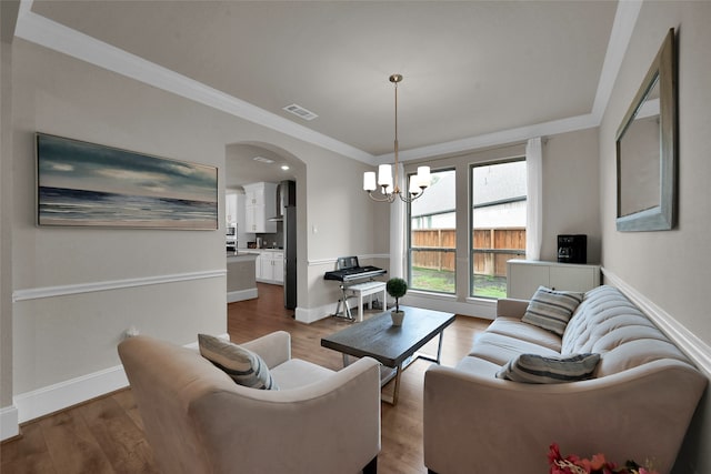 living room featuring wood-type flooring, ornamental molding, and a notable chandelier