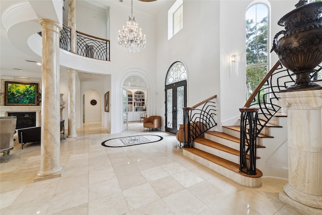 tiled foyer featuring decorative columns, a towering ceiling, a notable chandelier, and a wealth of natural light