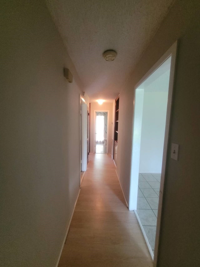 hall with built in features, a textured ceiling, and light hardwood / wood-style flooring