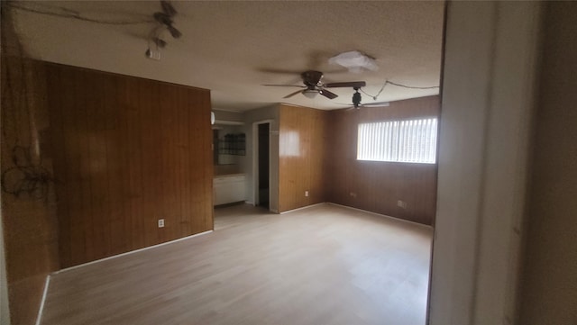 spare room with ceiling fan, wood walls, light hardwood / wood-style flooring, and a textured ceiling