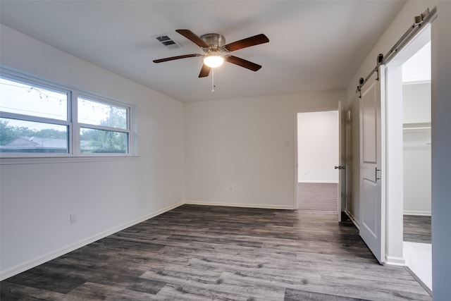 unfurnished bedroom with a barn door, ceiling fan, and dark wood-type flooring