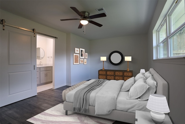 bedroom featuring ensuite bath, ceiling fan, dark wood-type flooring, sink, and a barn door