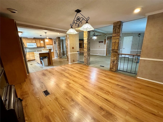 unfurnished dining area featuring a textured ceiling, decorative columns, light hardwood / wood-style flooring, crown molding, and ceiling fan