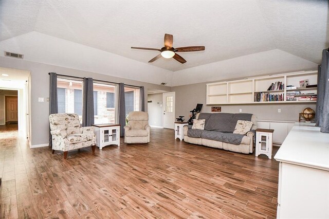 living room with light hardwood / wood-style flooring, a textured ceiling, lofted ceiling, a tray ceiling, and ceiling fan