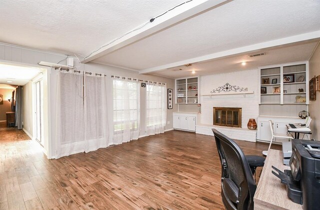 office with a textured ceiling, hardwood / wood-style flooring, a brick fireplace, brick wall, and beamed ceiling