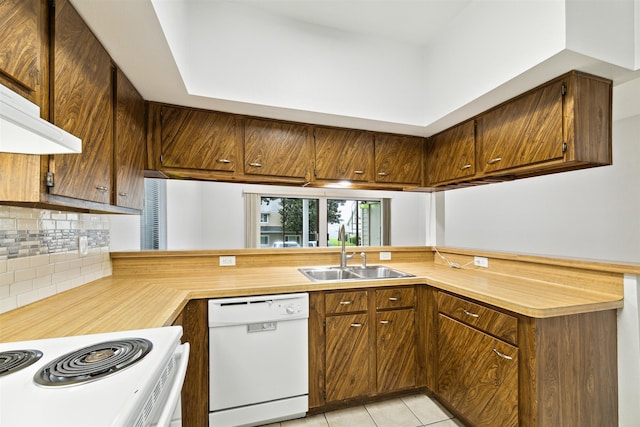 kitchen featuring light tile patterned flooring, tasteful backsplash, kitchen peninsula, white dishwasher, and sink