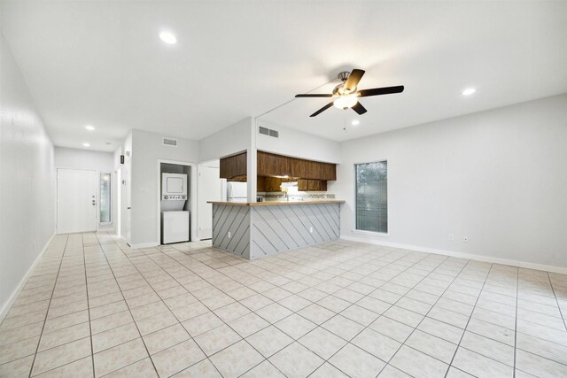 unfurnished living room featuring ceiling fan, stacked washing maching and dryer, and light tile patterned floors