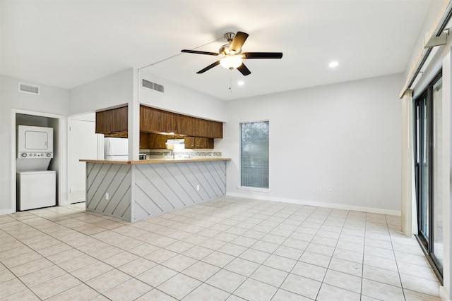 kitchen featuring light tile patterned floors, stacked washing maching and dryer, kitchen peninsula, a kitchen breakfast bar, and white refrigerator