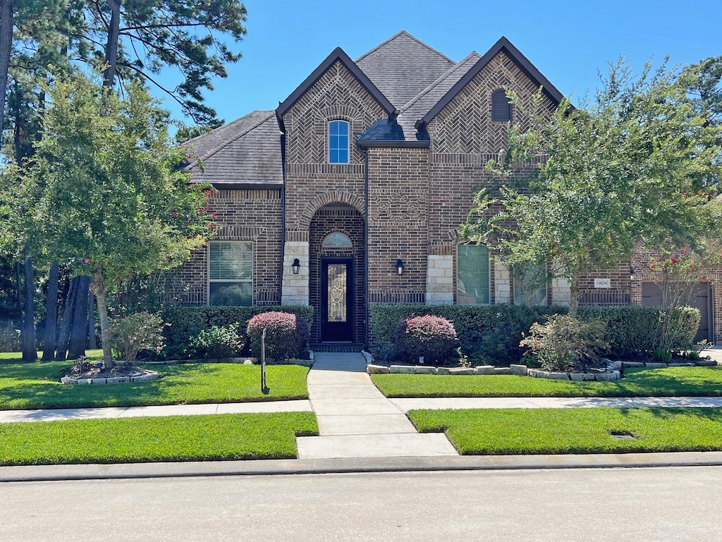 view of front facade featuring a front lawn, stone siding, brick siding, and roof with shingles