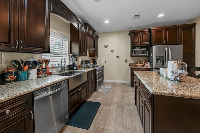 kitchen featuring dark brown cabinets, light stone counters, a kitchen island, appliances with stainless steel finishes, and light tile patterned floors