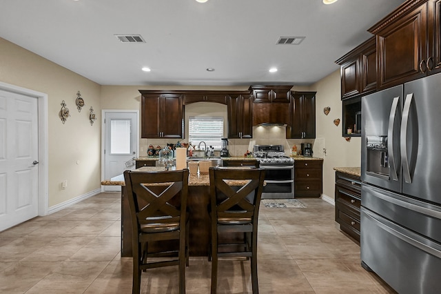 kitchen featuring appliances with stainless steel finishes, light stone countertops, dark brown cabinetry, and a kitchen island