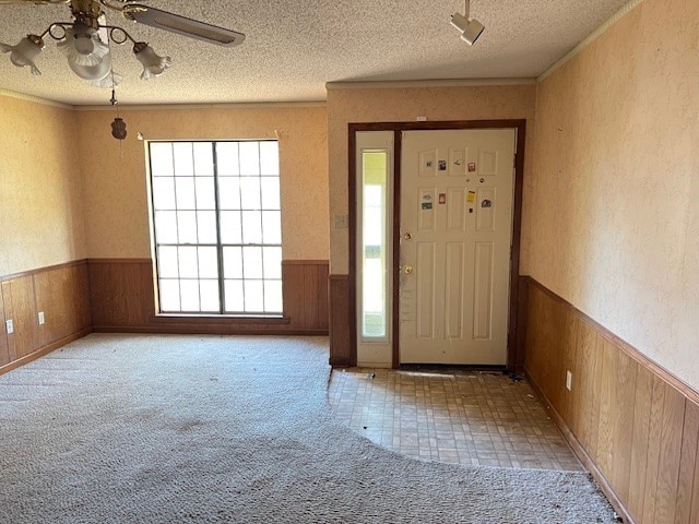 carpeted foyer entrance with ornamental molding, a textured ceiling, and wooden walls