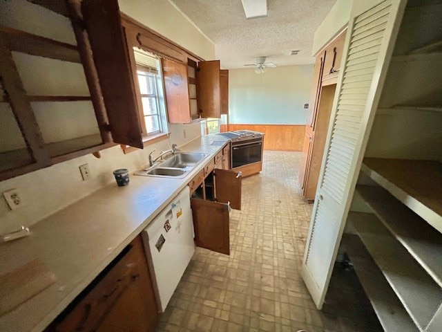 kitchen with ceiling fan, sink, wood walls, oven, and a textured ceiling