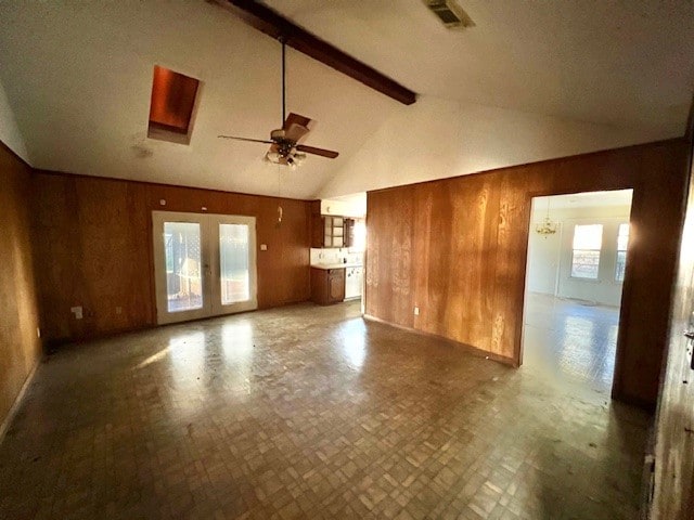 unfurnished living room featuring wooden walls, beamed ceiling, ceiling fan with notable chandelier, and high vaulted ceiling