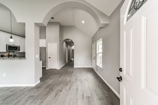 interior space featuring light stone counters, light hardwood / wood-style flooring, high vaulted ceiling, and white cabinetry