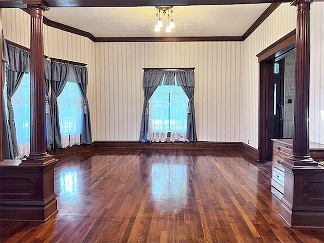 spare room featuring dark wood-type flooring, ornamental molding, and ornate columns