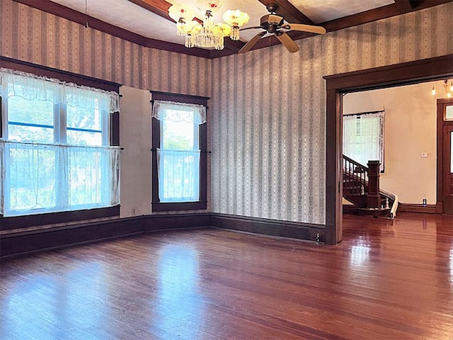 unfurnished room with ceiling fan with notable chandelier, beam ceiling, and dark hardwood / wood-style flooring