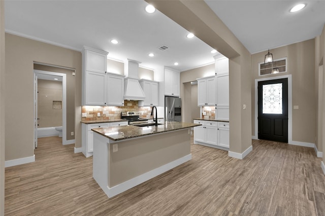 kitchen featuring stainless steel appliances, sink, dark stone countertops, tasteful backsplash, and a center island with sink