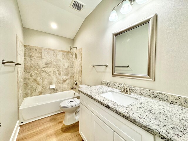 full bathroom featuring toilet, hardwood / wood-style floors, vanity, tiled shower / bath combo, and vaulted ceiling