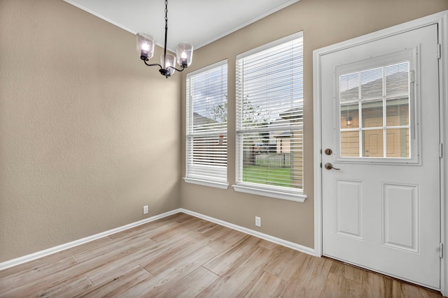 interior space featuring light wood-style floors, a textured wall, baseboards, and an inviting chandelier