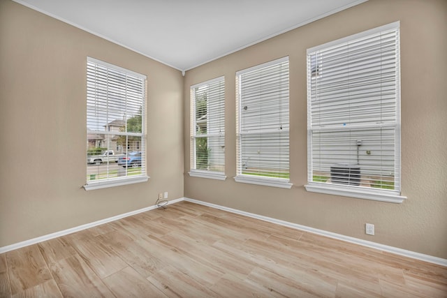 empty room with baseboards, ornamental molding, and light wood-style floors