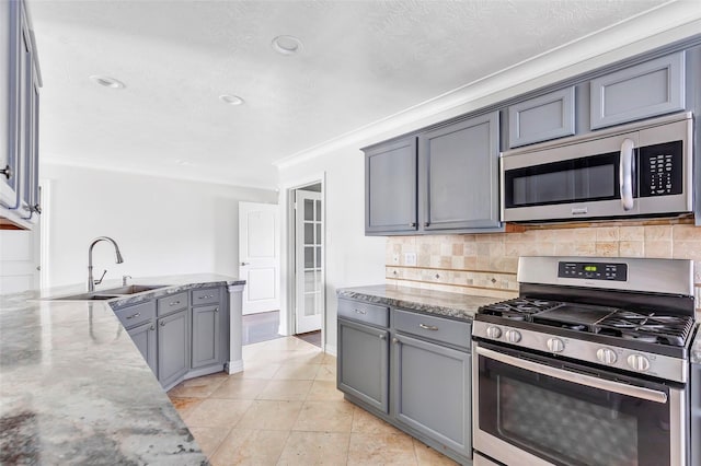 kitchen with decorative backsplash, gray cabinets, light stone countertops, and appliances with stainless steel finishes