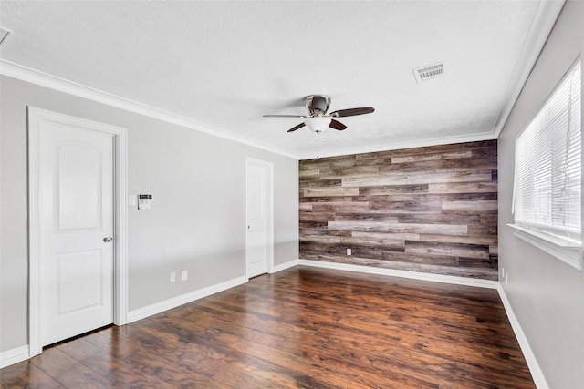 empty room featuring dark wood-type flooring, ceiling fan, ornamental molding, and wood walls