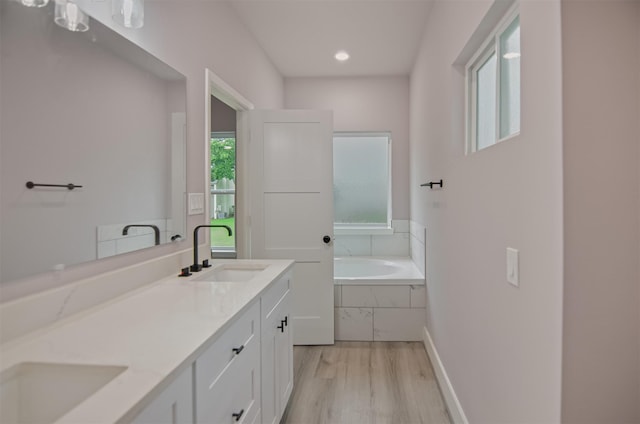 bathroom with hardwood / wood-style flooring, a relaxing tiled tub, and vanity