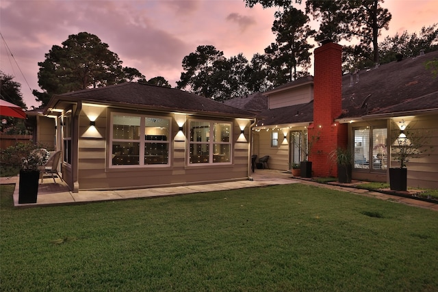 back house at dusk with a lawn