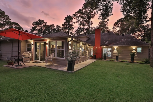 back house at dusk with a yard, a patio, and a sunroom