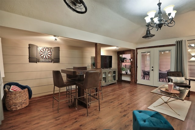 dining space with french doors, dark wood-type flooring, a chandelier, a textured ceiling, and wooden walls