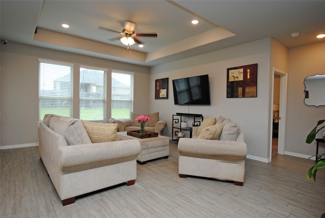 living room with light wood-type flooring, ceiling fan, and a raised ceiling