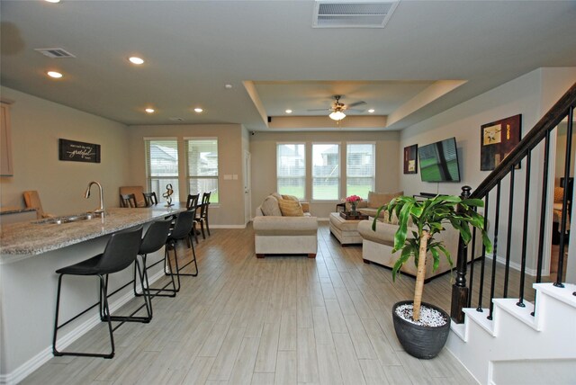 living room with sink, light hardwood / wood-style flooring, ceiling fan, and a raised ceiling